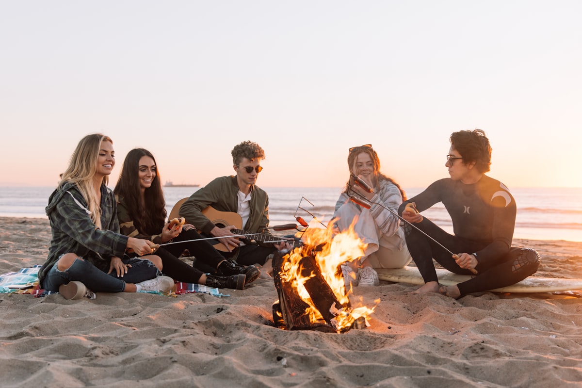 Friends playing guitar around a fire on the beach